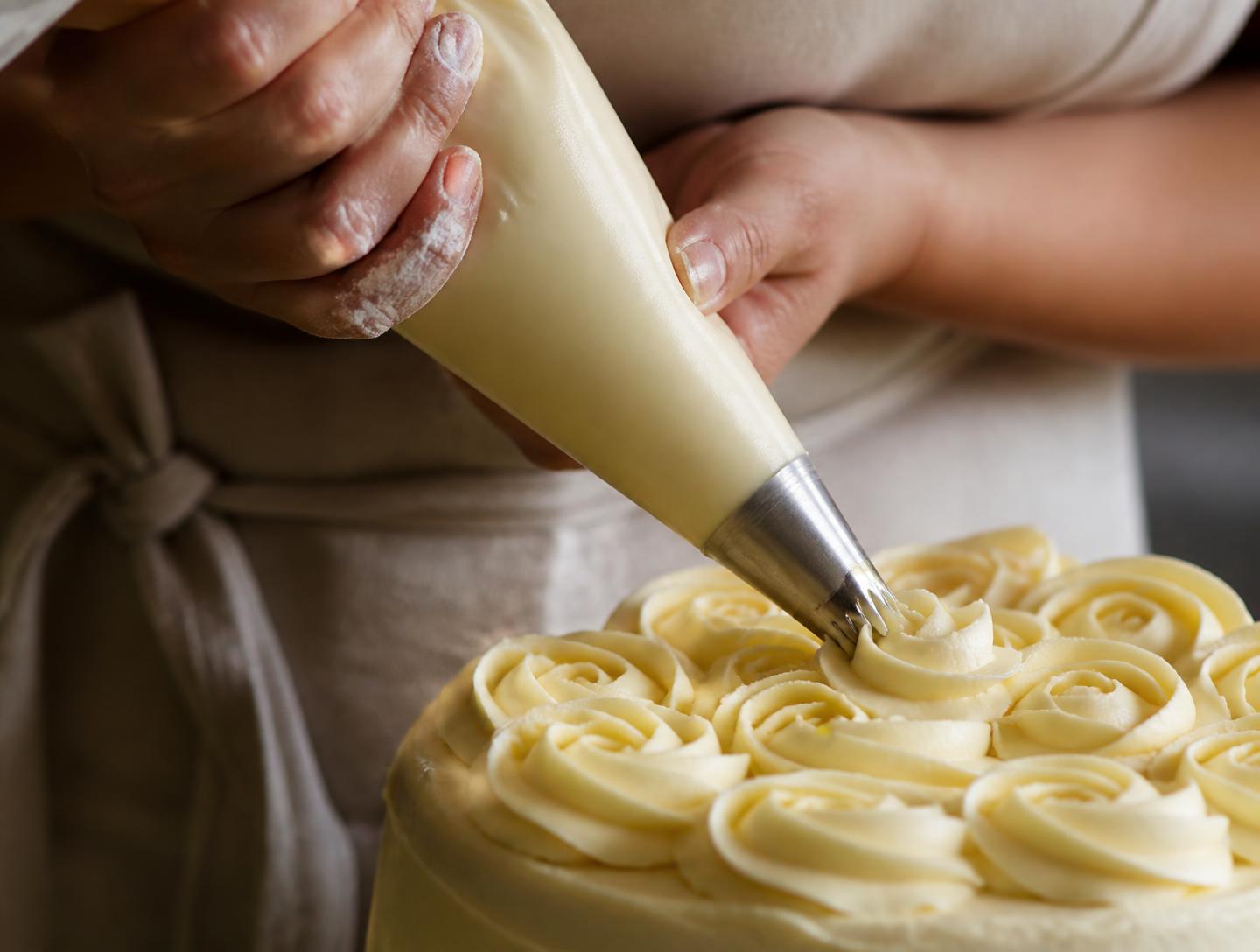Pastry chef hand-piping buttercream rosettes onto a GoodCake cake