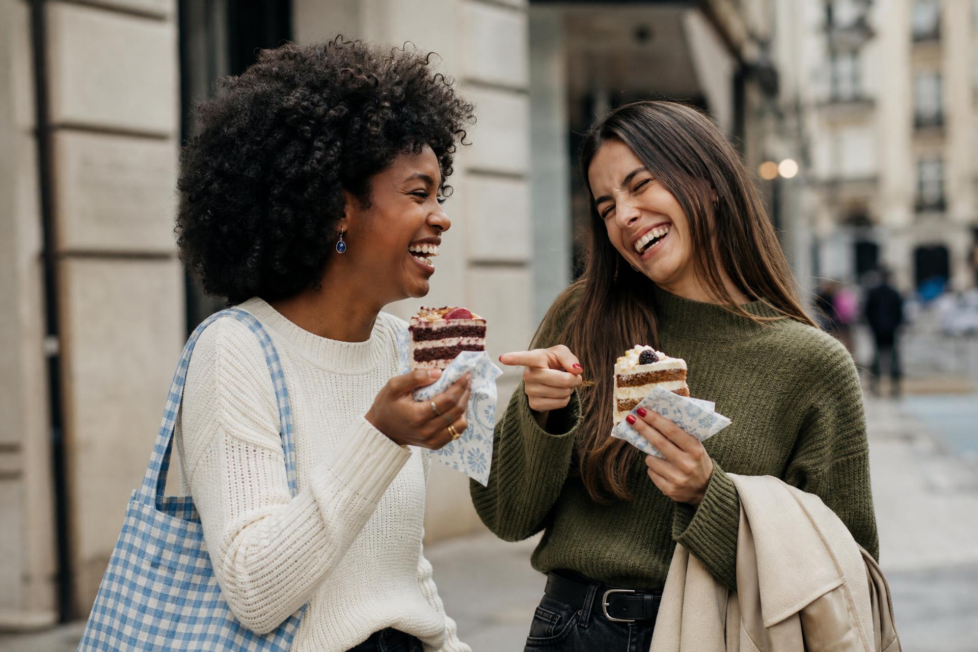 GoodCake luxury bakery campaign: two friends laughing on a Calgary street while eating slices of layered cake
